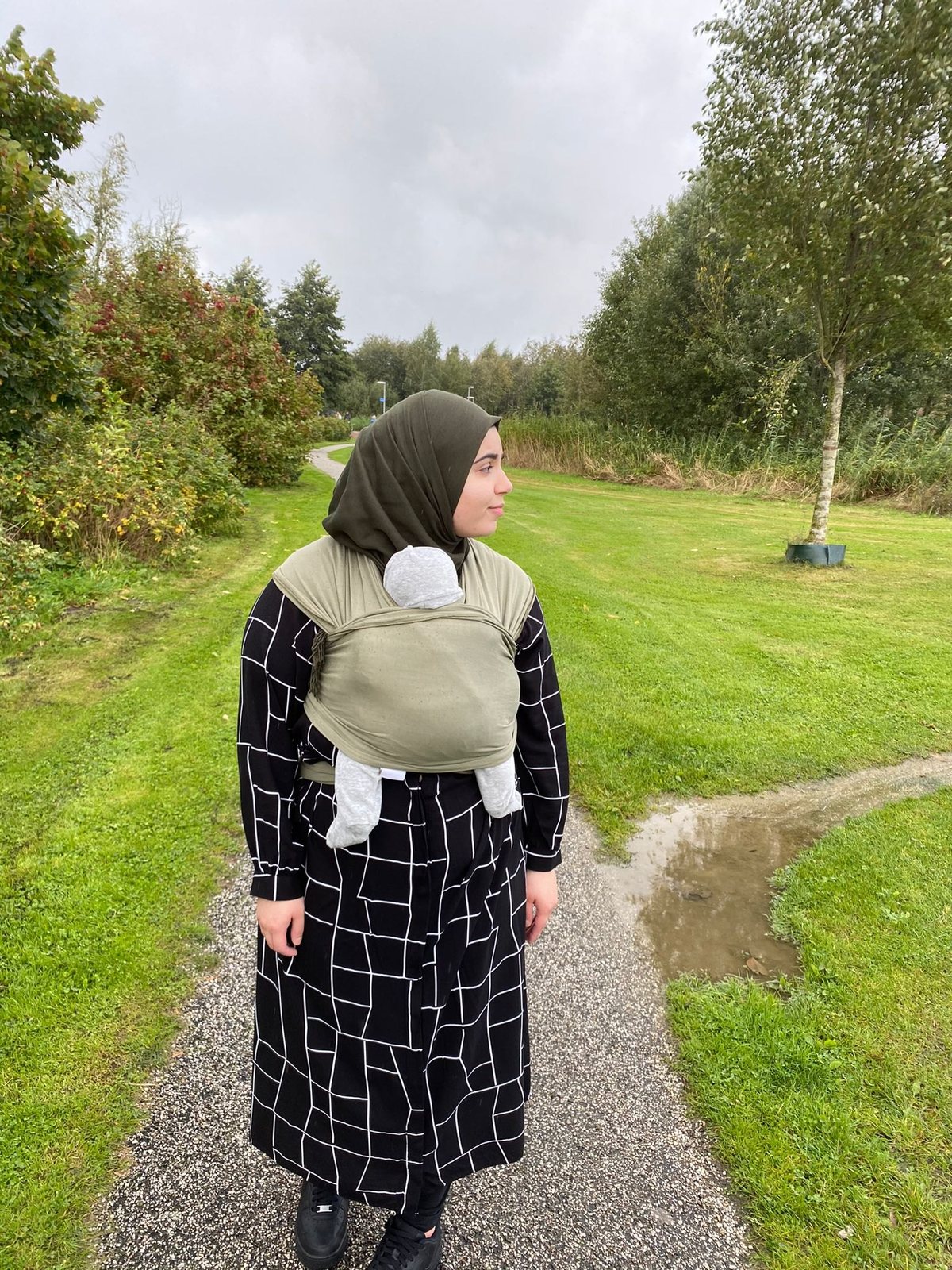 Kind in een groene draagzak op de rug, van achteren gezien