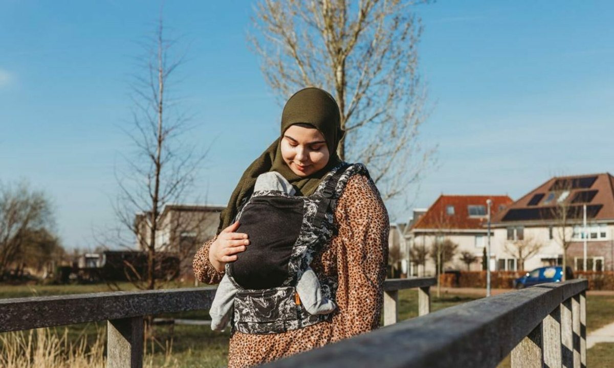 Feride draagt haar baby in een draagzak bij een houten hek