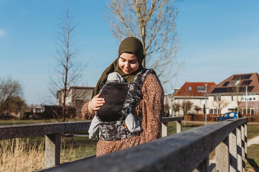 Feride kijkt naar haar baby die zij in een draagzak draagt, buiten in de zon
